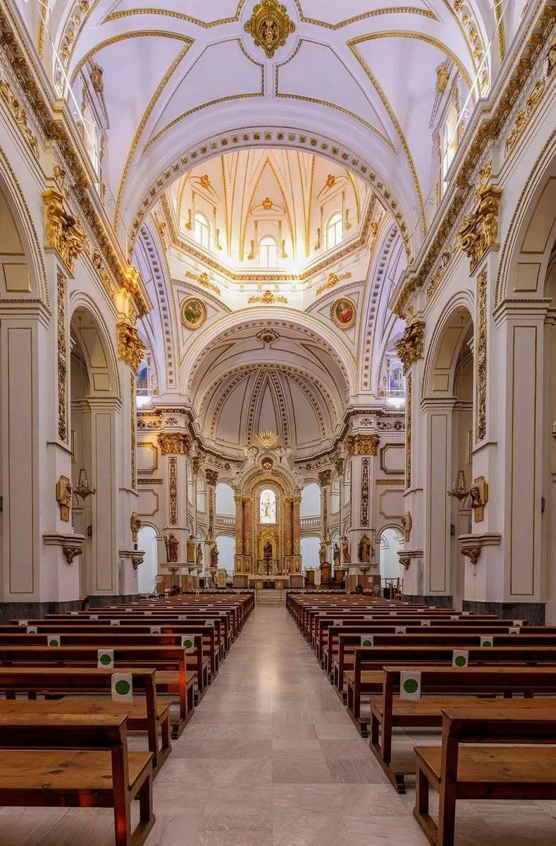 La nave central de la parroquia hacia el altar mayor, con bóveda de cañón, cornisas doradas y la cúpula sobre el crucero
