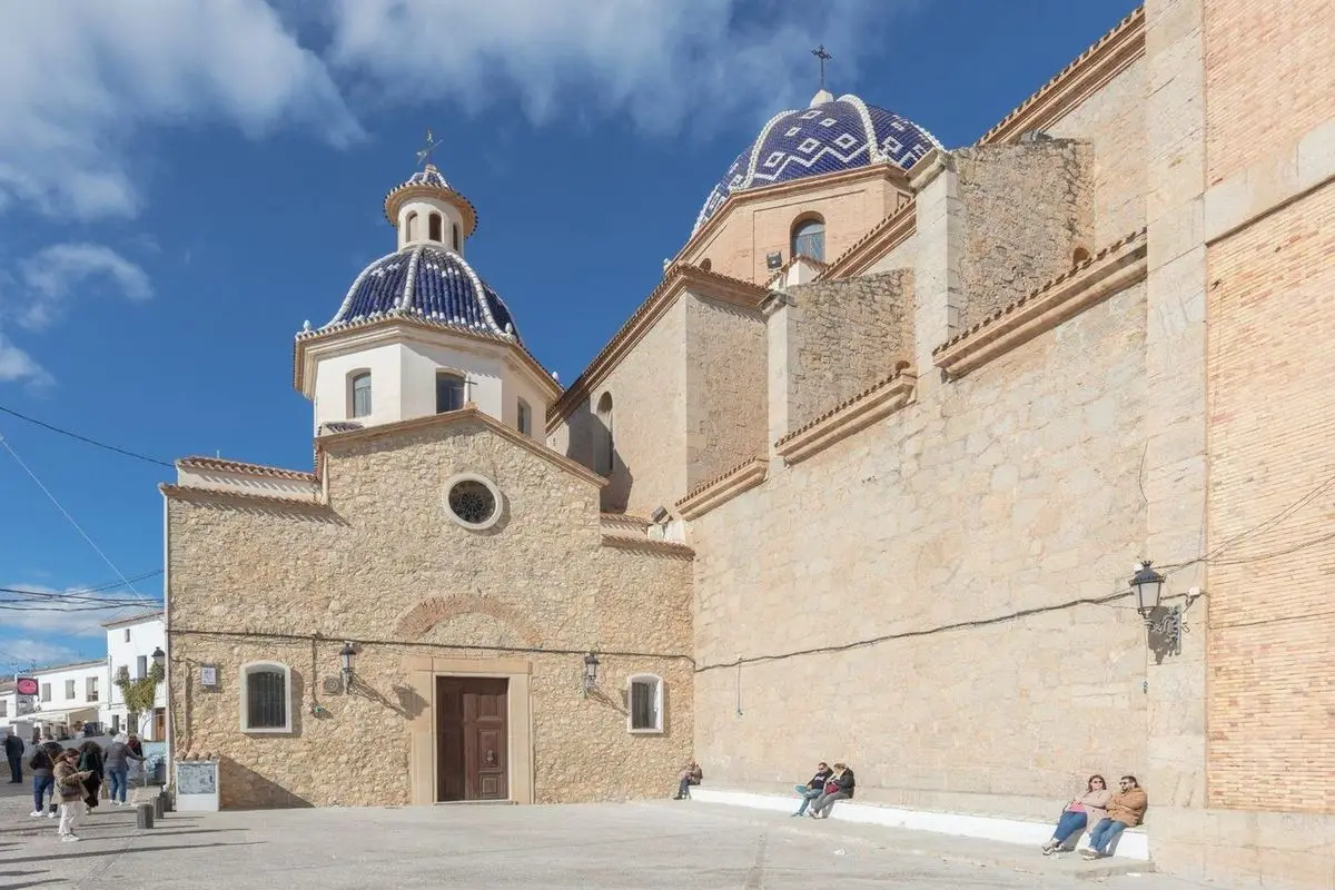 La parroquia de lado: dos cúpulas de escama azul y blanca sobre muros de mampostería y, delante, el cuerpo más bajo con su rosetón