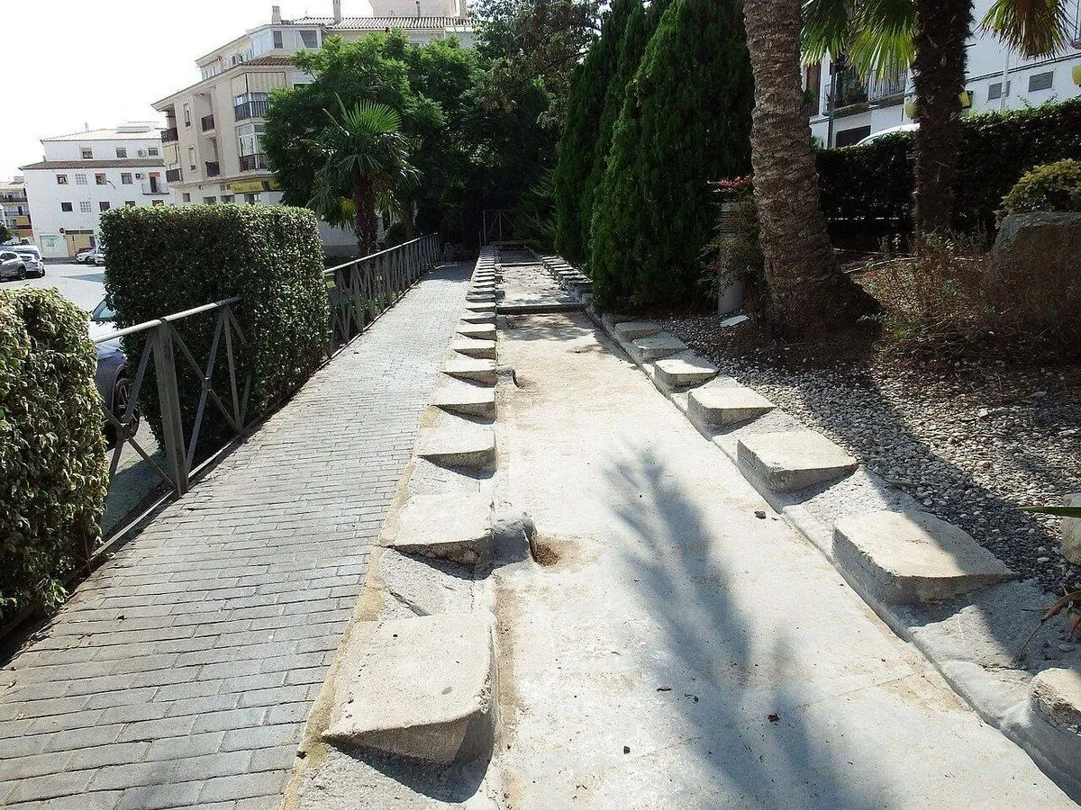 El lavadero de Garganes: una pila larga con las piedras inclinadas de lavar a ambos lados, rodeado de setos y viviendas