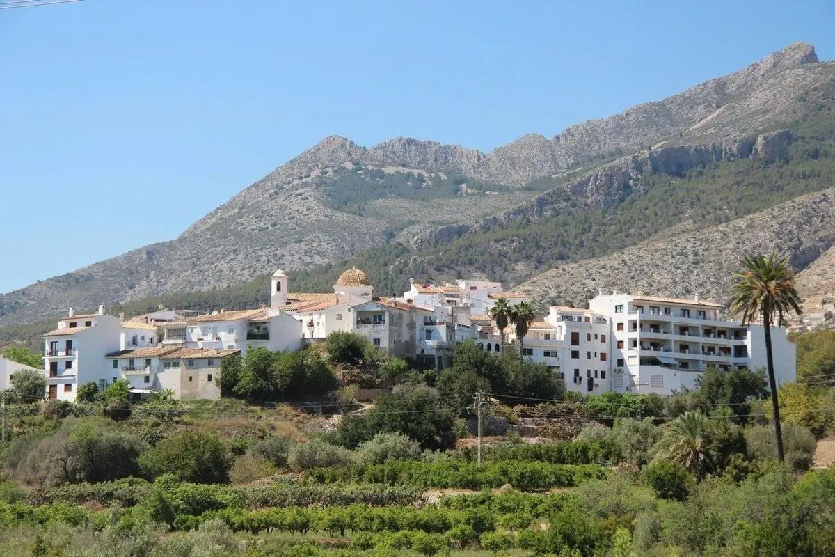Altea la Vella en la ladera sobre los huertos; en el centro, una iglesia con cúpula de escama y campanario estrecho, y detrás la sierra