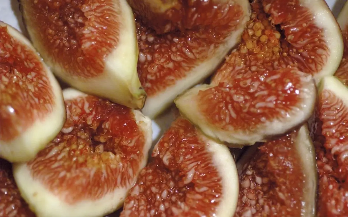 Higos abiertos, muy juntos: piel clara y, dentro, pulpa roja y granulosa llena de pepitas.