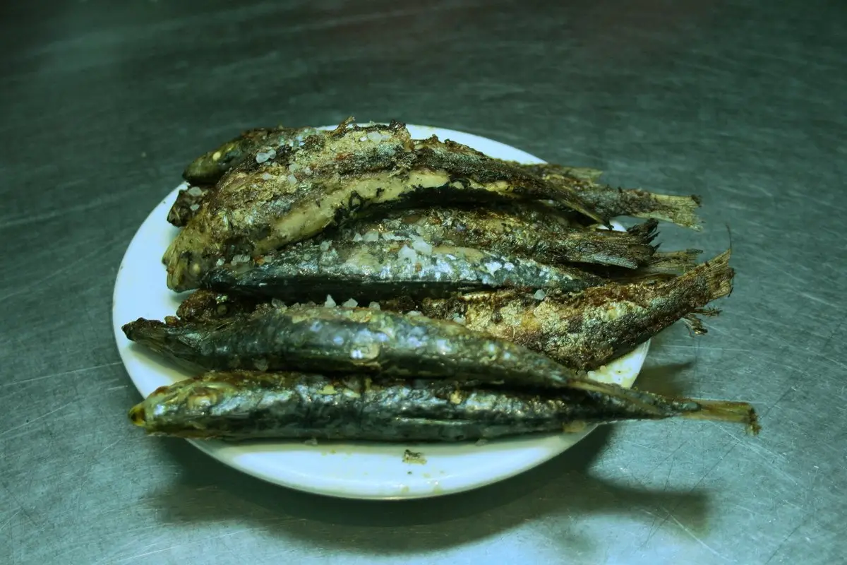 Un plato pequeño con siete sardinas a la plancha, de piel plateada y tostada, con sal gorda, sobre una barra de acero.