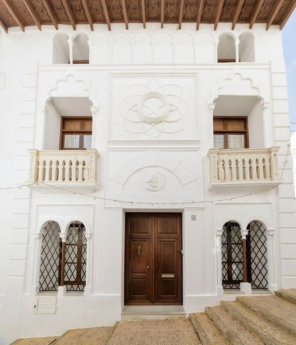 La fachada de frente: dos balcones de balaustres torneados bajo arcos lobulados, encima una arquería y un alero de madera tallada; sobre la puerta, un medallón con el nombre de Cervantes